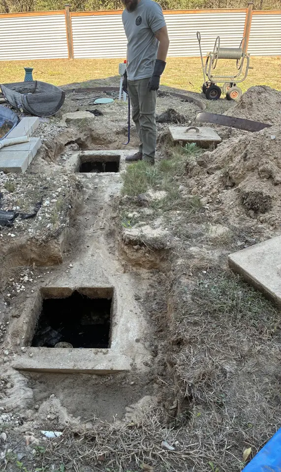 Septic tank lids uncovered in a dug-out yard, with the technician standing beside the excavation