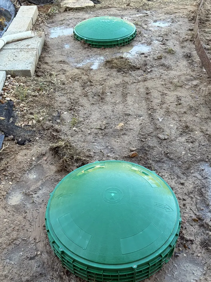 Two new green septic riser lids set at ground level in a freshly graded yard