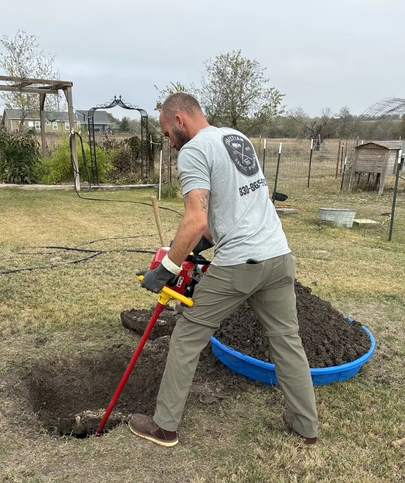 Technician using a red soil probe beside a dug hole while locating a buried septic tank